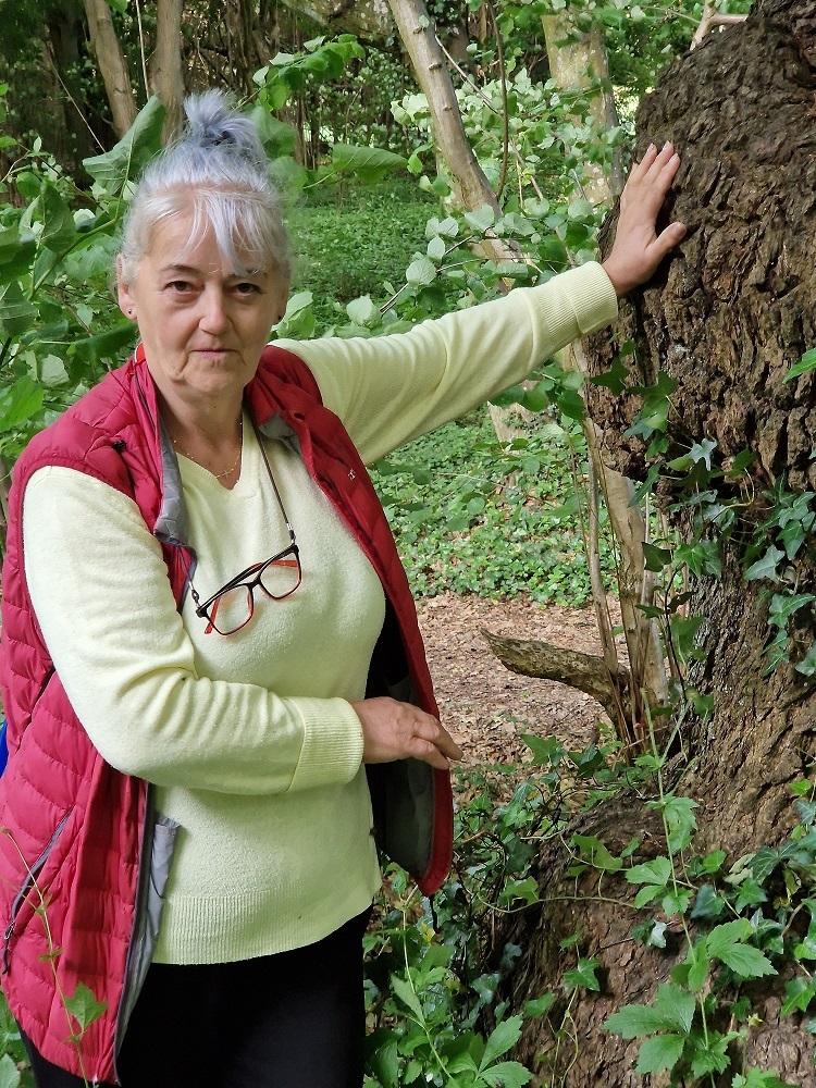 uczestniczka Klubu seniora w lesie opierająca się lewą ręką o drzewo