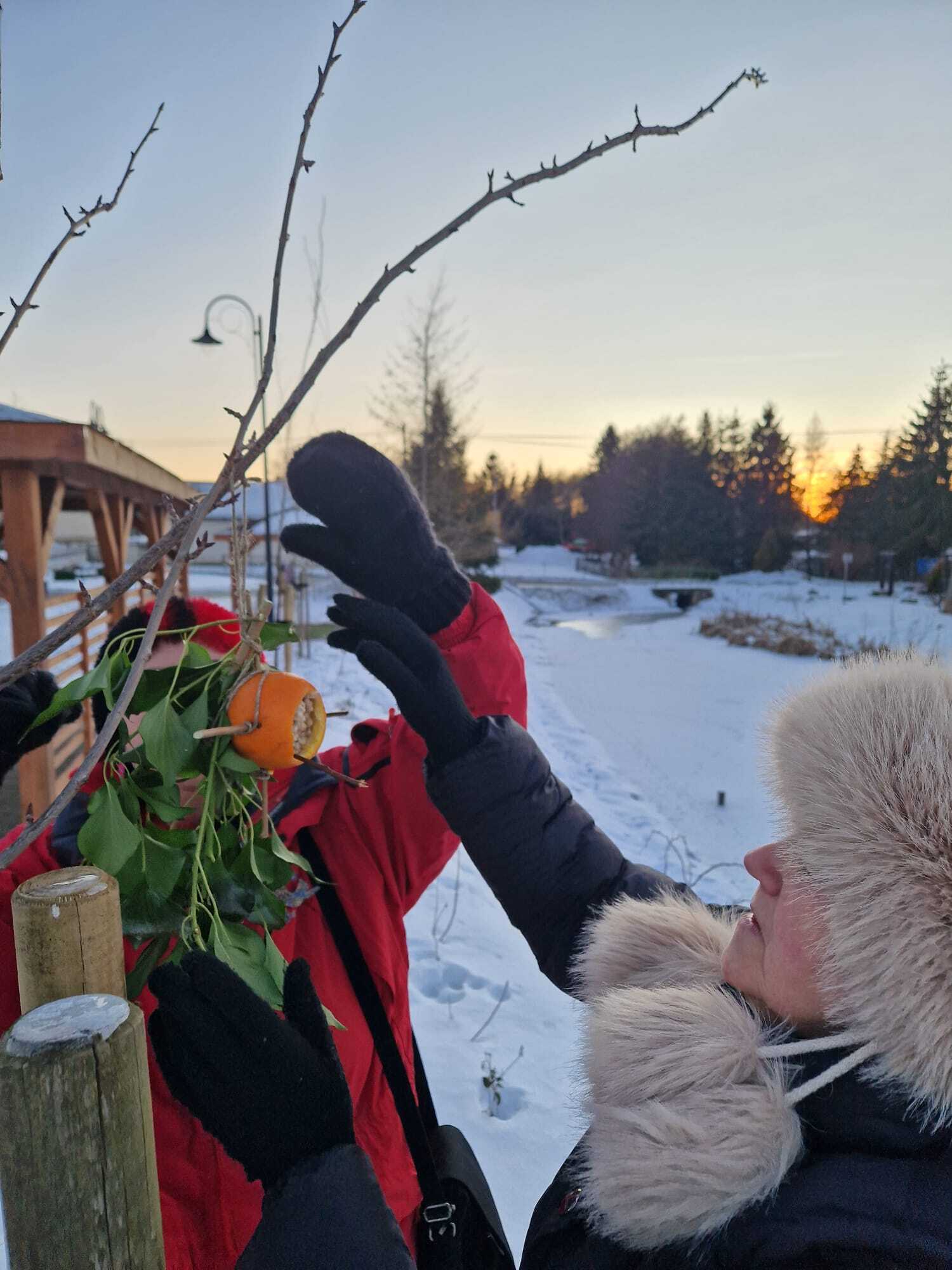 dwie uczestniczki warsztatów wieszające gotowy karmnik z gałązek na zewnątrz