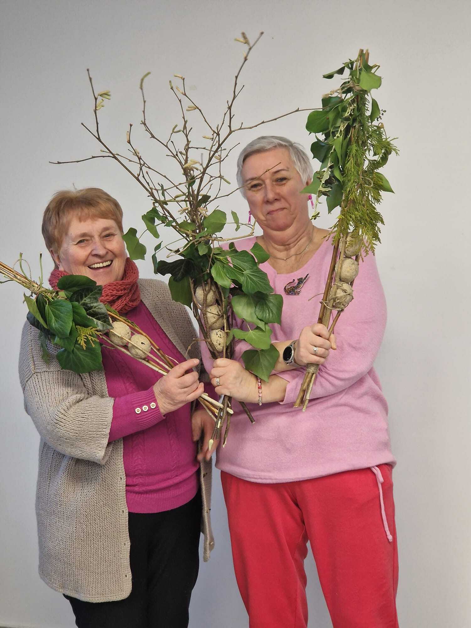 dwie uczestniczki warsztatów stojące przy sobie prezentujące w dłoniach gotowe karmniki dla ptaków stworzone z gałązek