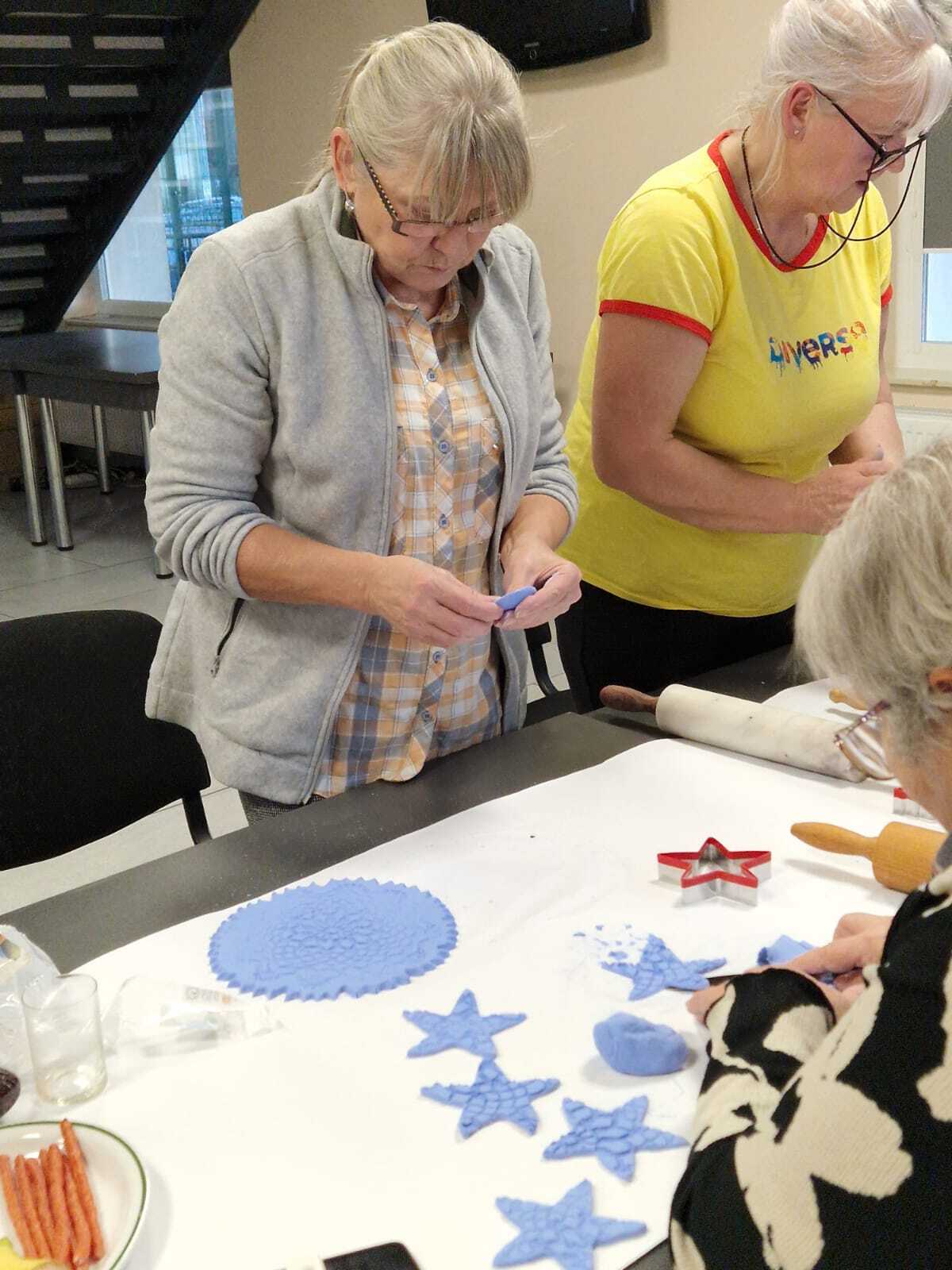 trzy uczestniczki warsztatów przy wspólnym stole tworzące ozdoby ceramiczne