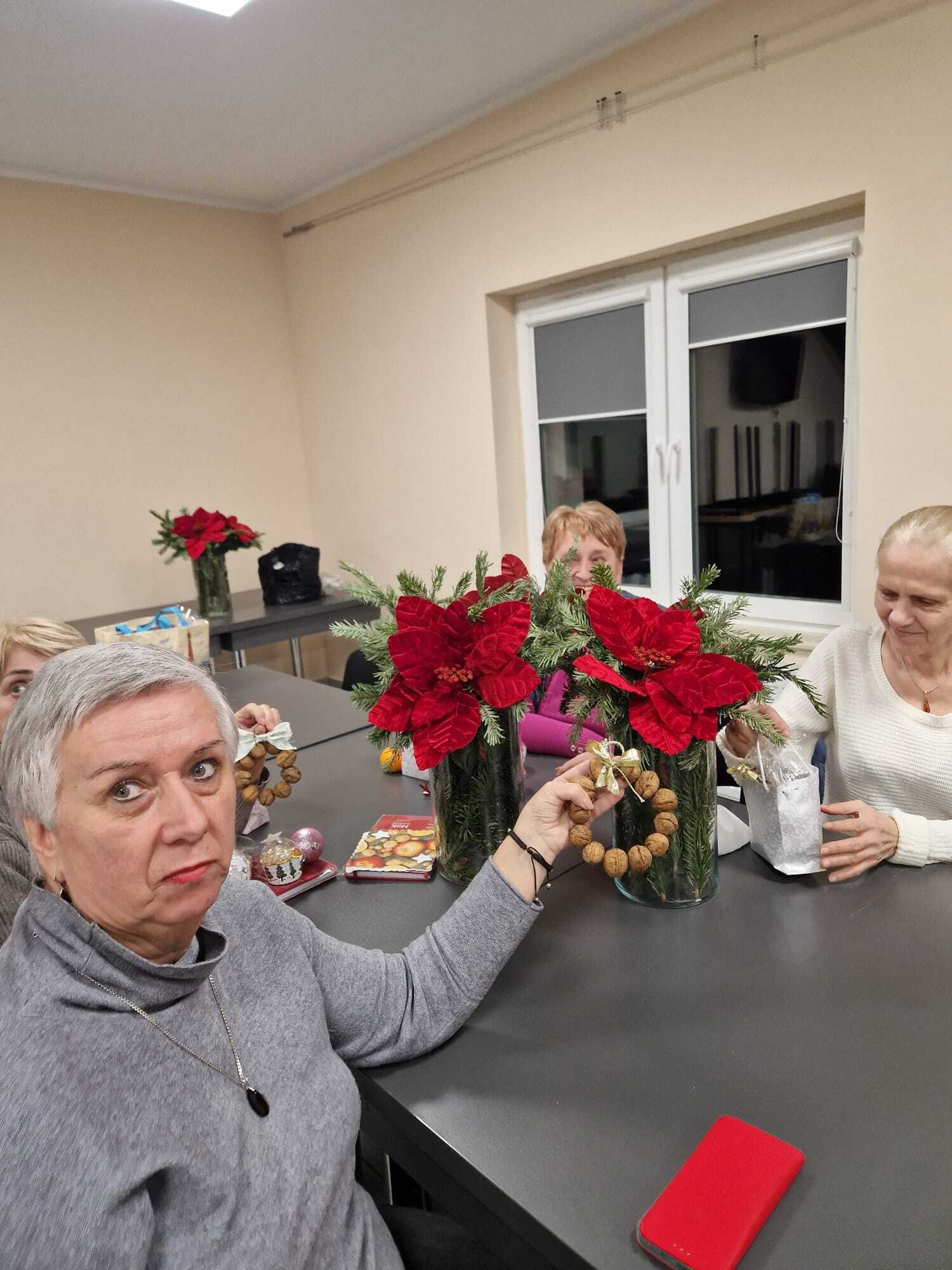 uczestniczka warsztatów siedząca przy stole prezentująca w dłoni gotową ozdobę z orzechów włoskich