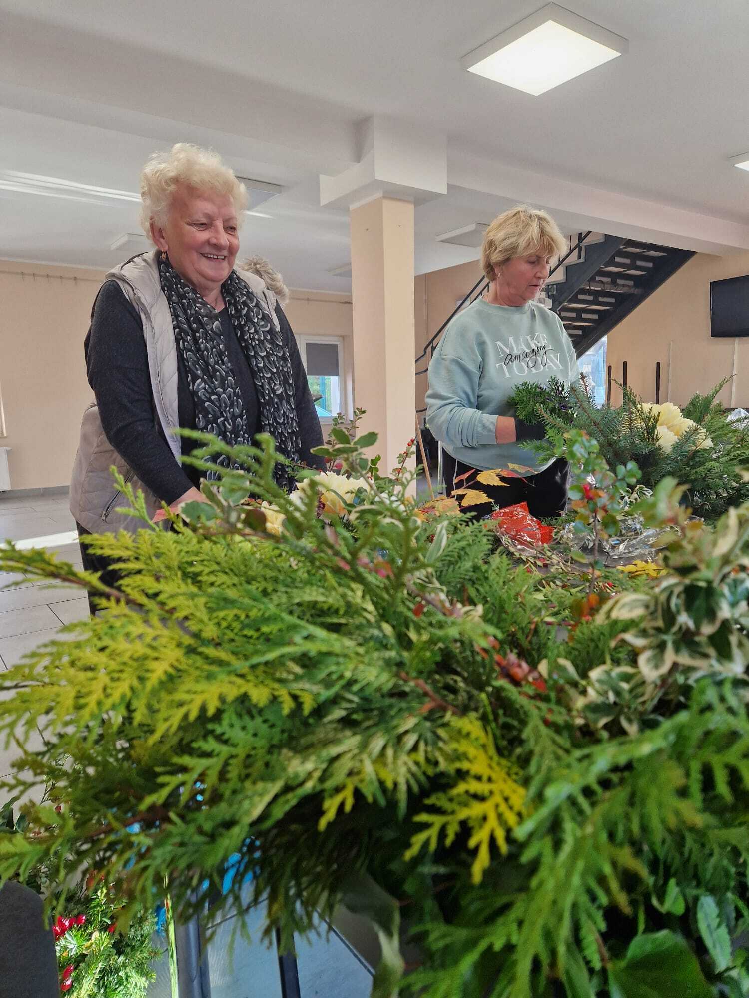 dwie uczestniczki warsztatów stojące przy stole i wykonujące stroiki