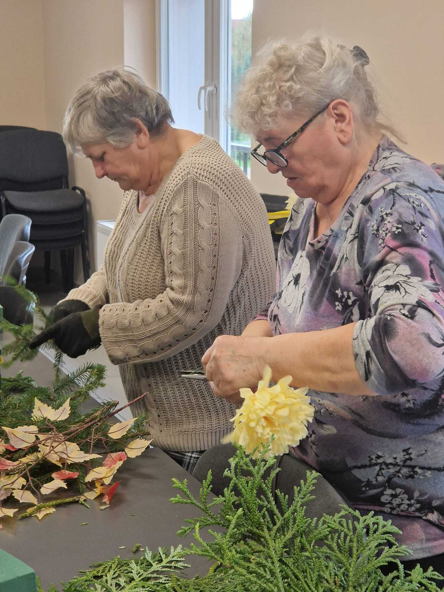 dwie uczestniczki warsztatów stojące przy stole wykonujące stroiki