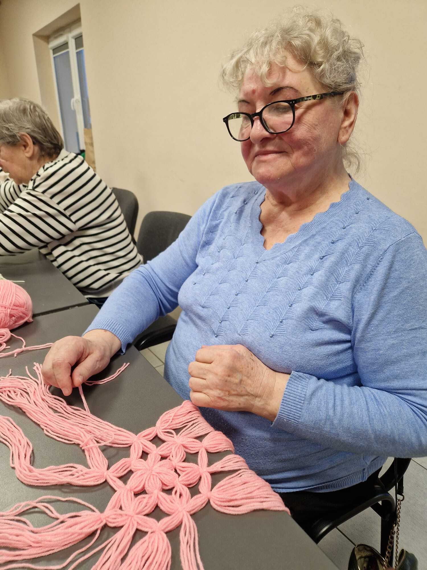 uczestniczka warsztatów siedząca przy stole w trakcie plecienia ozdoby z włóczki