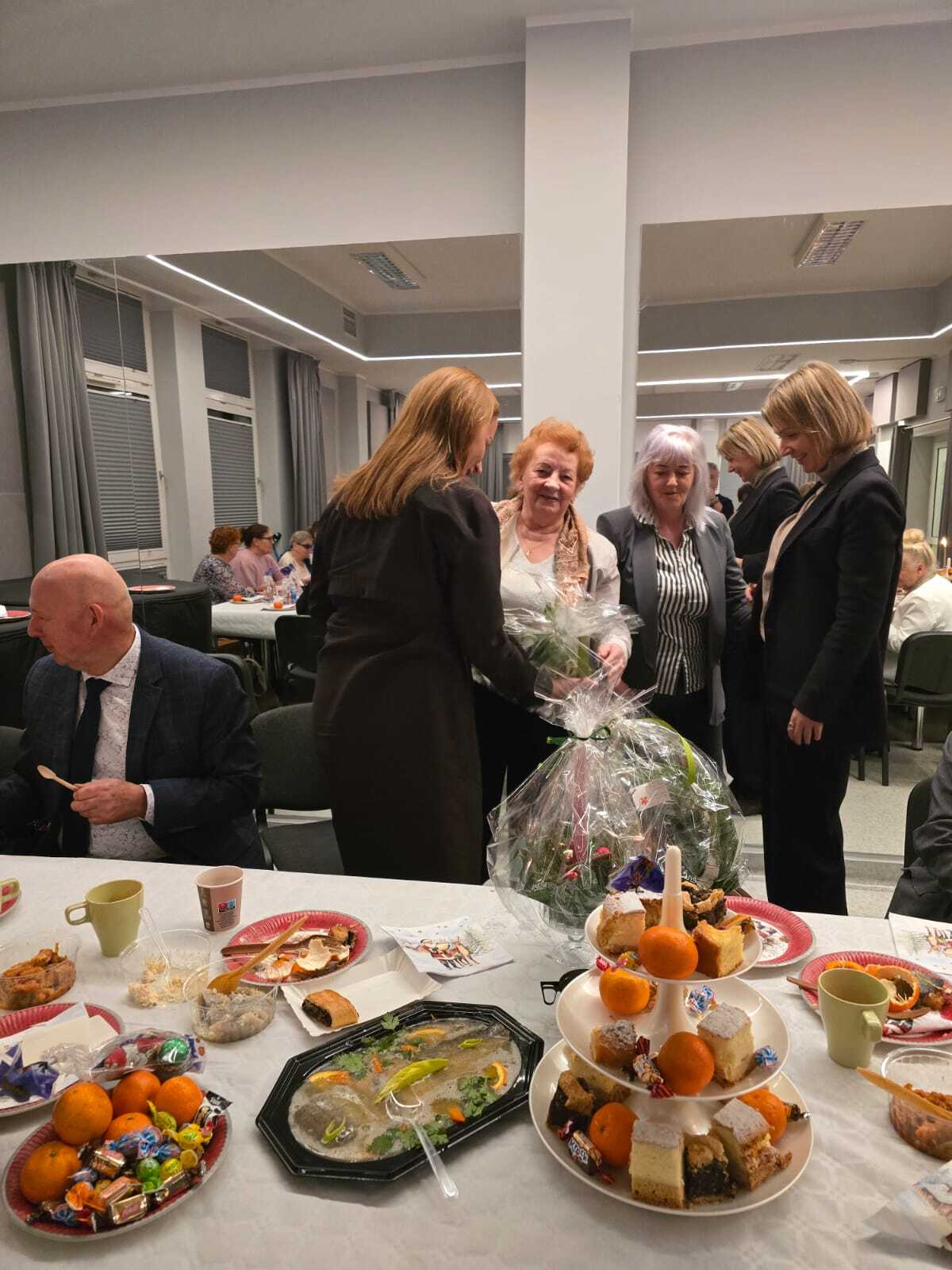 dwie uczestniczki Klubu Seniora przy stole wigilijnym składające podziękowania, życzenia dla Pani Burmistrz i Pani Skarbnik Kobylnicy