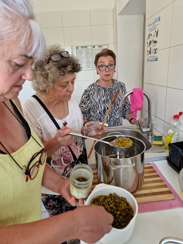 zdjęcie ptrzedstawia trzy uczestniczki warsztatów cedzące z garnka ugotowane zioła